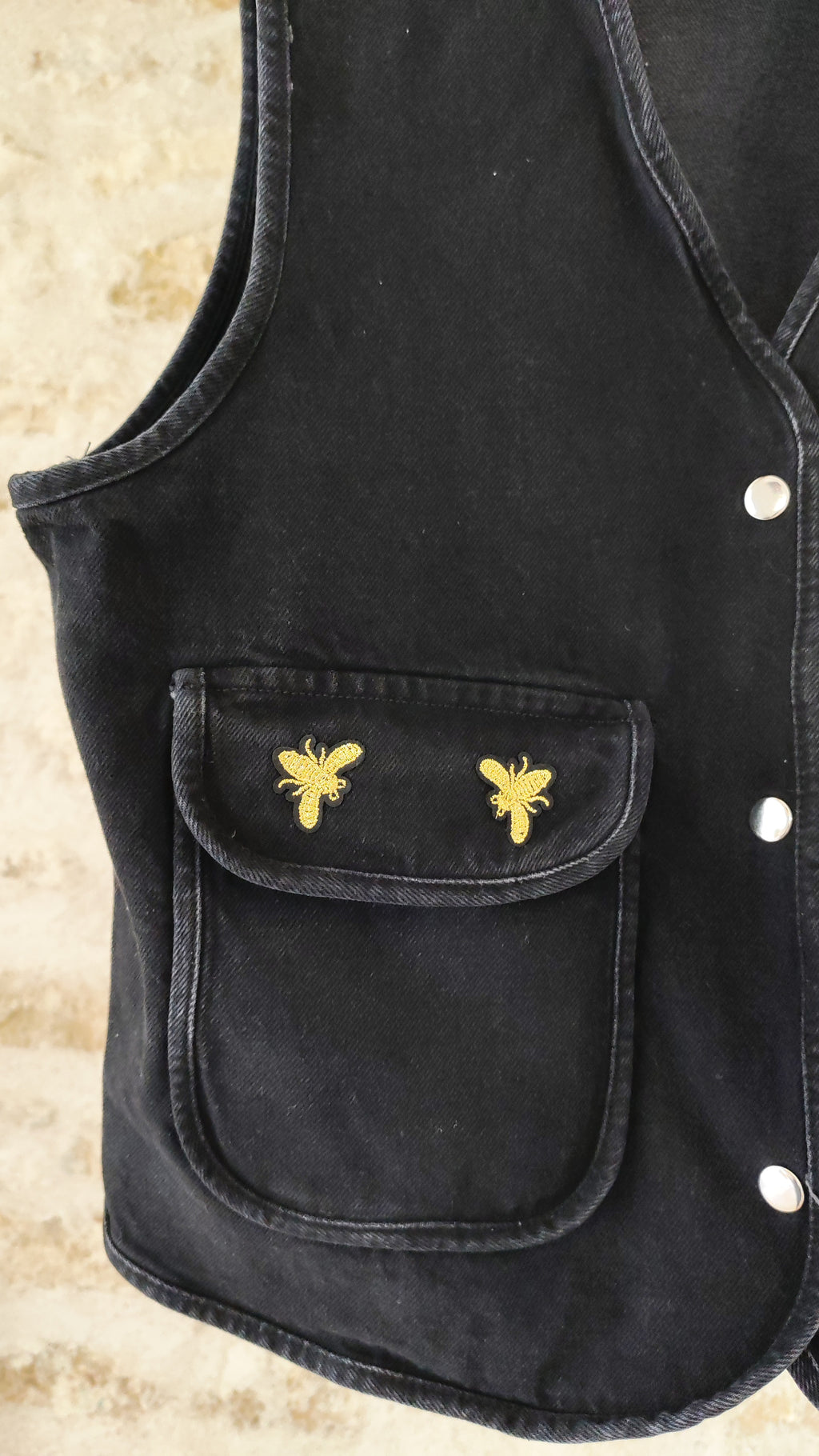 Veste sans manches noire avec écussons abeilles dorés – vue dos sur cintre – BFunny