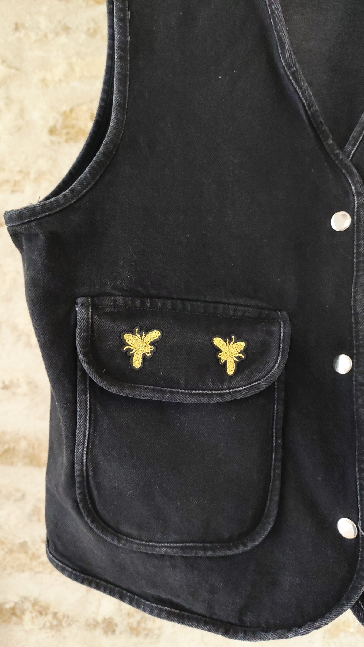 Veste sans manches noire avec écussons abeilles dorés – vue dos sur cintre – BFunny