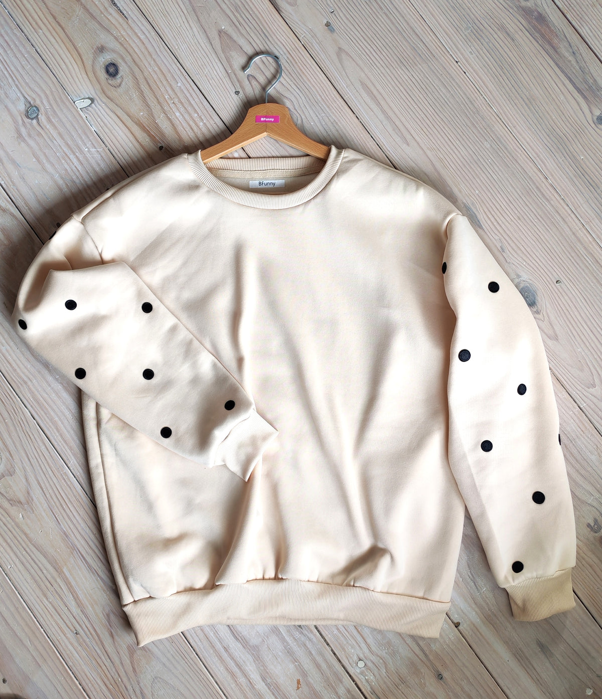 Détail du sweat beige pois noirs BFunny sur cintre, zoom sur les écussons brodés sur la manche
