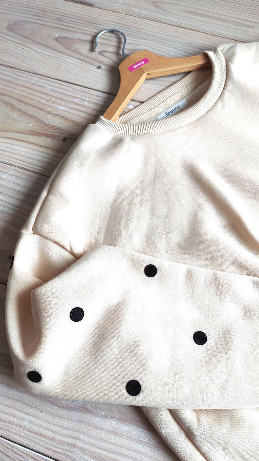 Détail du sweat beige pois noirs BFunny sur cintre, zoom sur les écussons brodés sur la manche