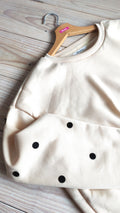 Détail du sweat beige pois noirs BFunny sur cintre, zoom sur les écussons brodés sur la manche