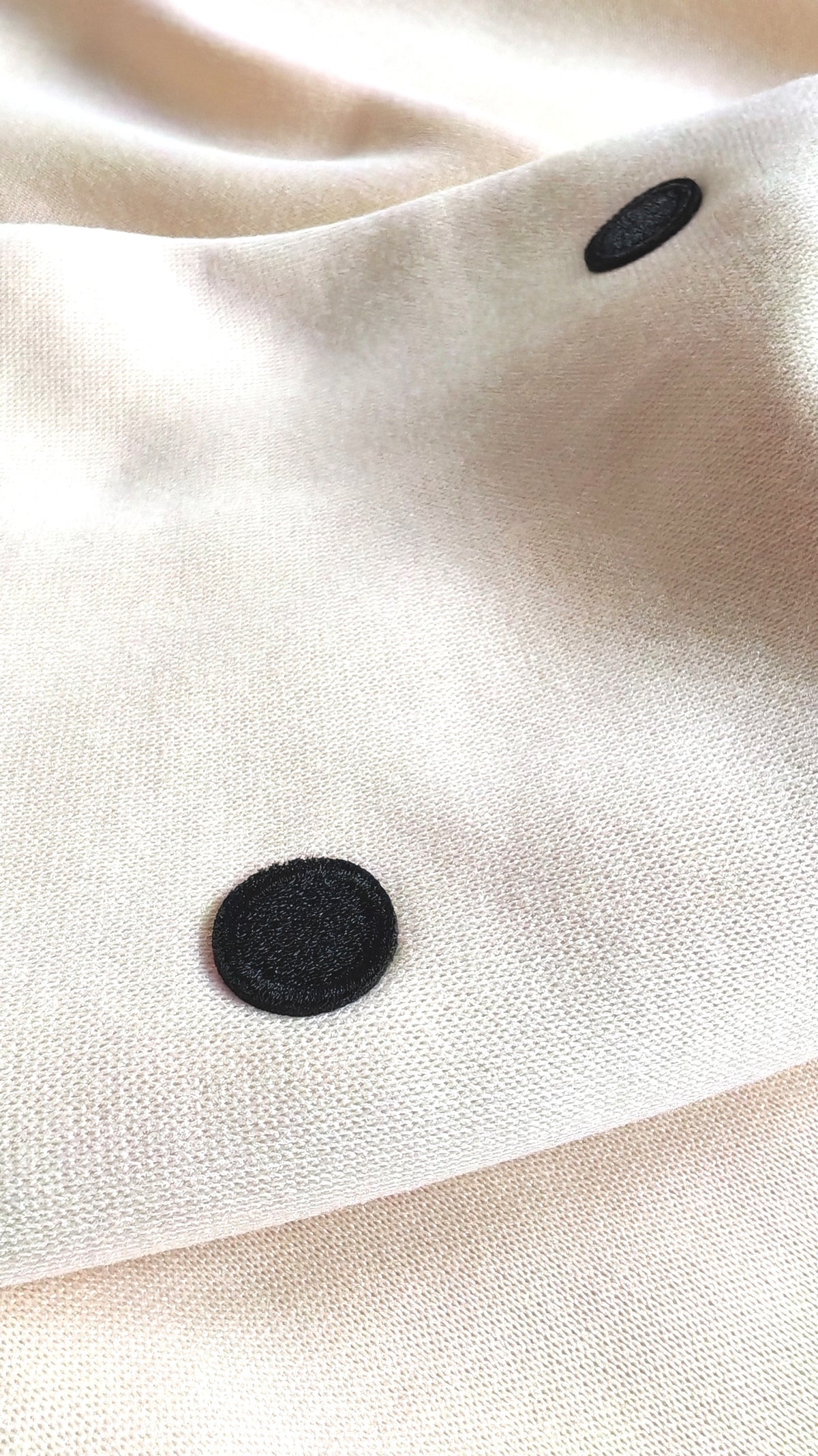 Gros plan sur un écusson pois noir brodé sur tissu beige — détail signature du Sweat beige pois noirs BFunny