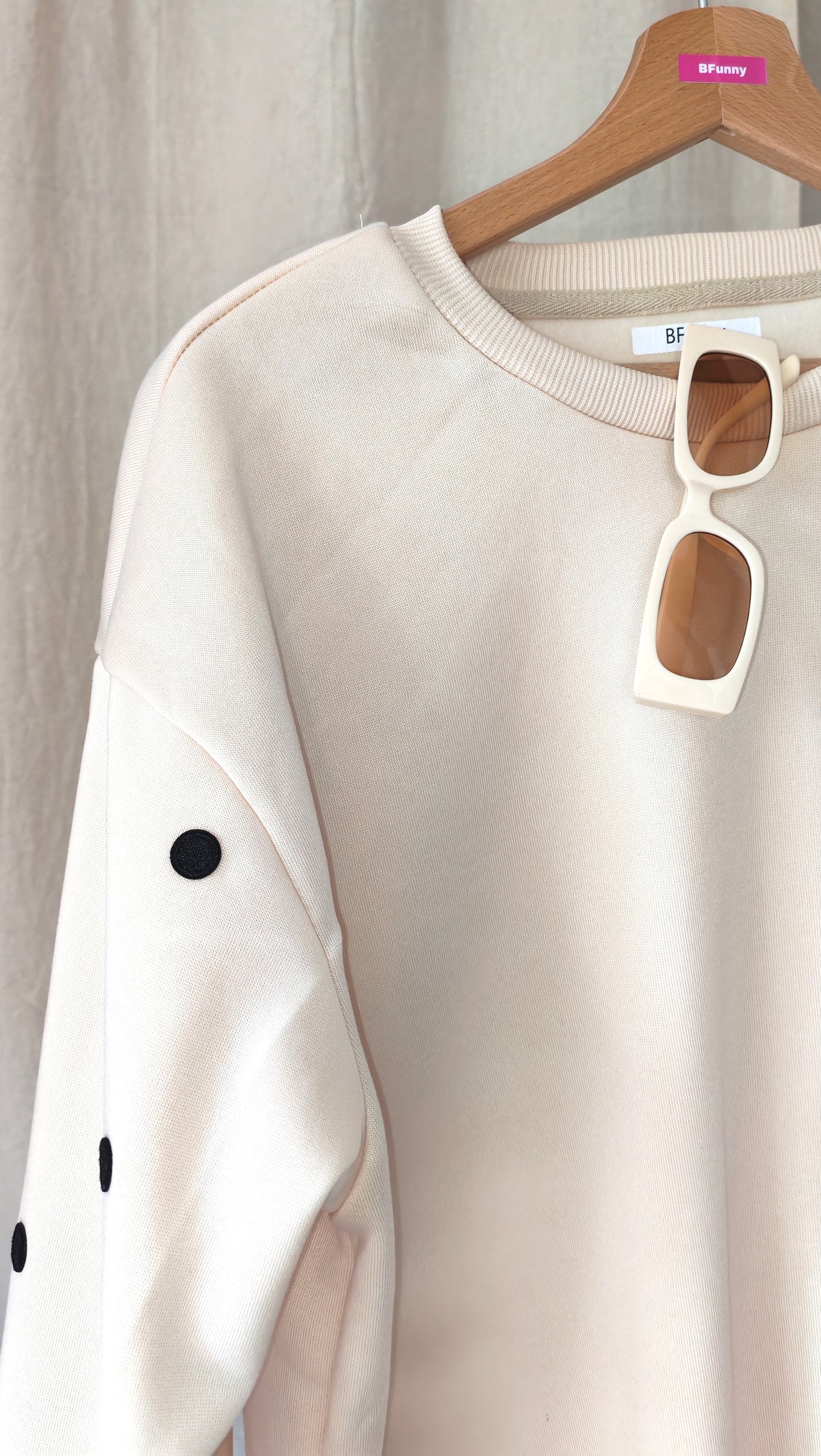 Détail du sweat beige pois noirs BFunny sur cintre, zoom sur les écussons brodés sur la manche